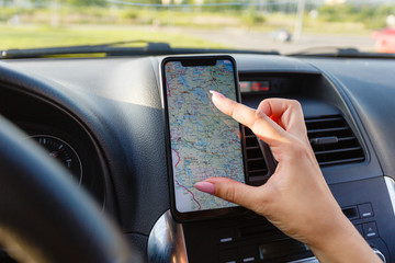 Close-up of woman using GPS navigation in mobile phone while driving car at sunset. The female hand changes the size of the image on the smartphone with a gesture of two fingers.