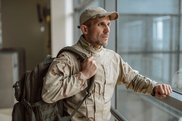 Waist up of calm American soldier in camouflage standing at the window