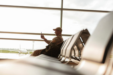 Side view of American soldier in camouflage looking at screen of smartphone