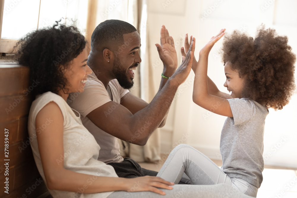 African kid daughter give high-five to daddy playing with parents - obrazy, fototapety, plakaty 
