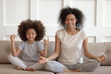 Healthy African Mother Teaching Meditation Sit With Daughter On Sofa