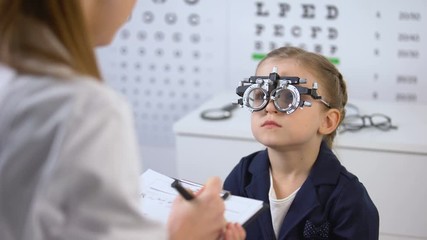 Poster - Cute girl in optical trial frame waiting prescription from ophthalmologist