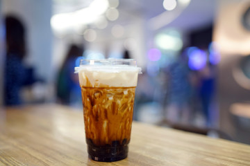 Bubble Milk Tea - A plastic glass of fresh milk with black sugar syrup (Kuromitsu) and hot black pearl (Boba) topped with cream cheese on blurred background, Taiwanese drinking culture.