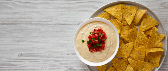 Homemade cheesy dip in a bowl, yellow tortilla chips, overhead view. Top view, from above, flat lay. Copy space.