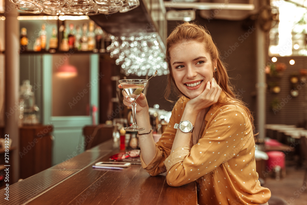Smiling woman holding martini drink sitting at the bar counter - obrazy, fototapety, plakaty 