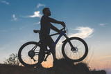 Fototapeta  - Cyclist in shorts and jersey on a modern carbon hardtail bike with an air suspension fork rides off-road on the orange-red hills at sunset evening in summer	