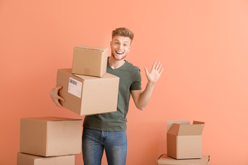 Young man with cardboard boxes on color background