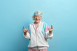 © alfa27 - Cute hipster grandmother smiling and making rock sign against blue studio background