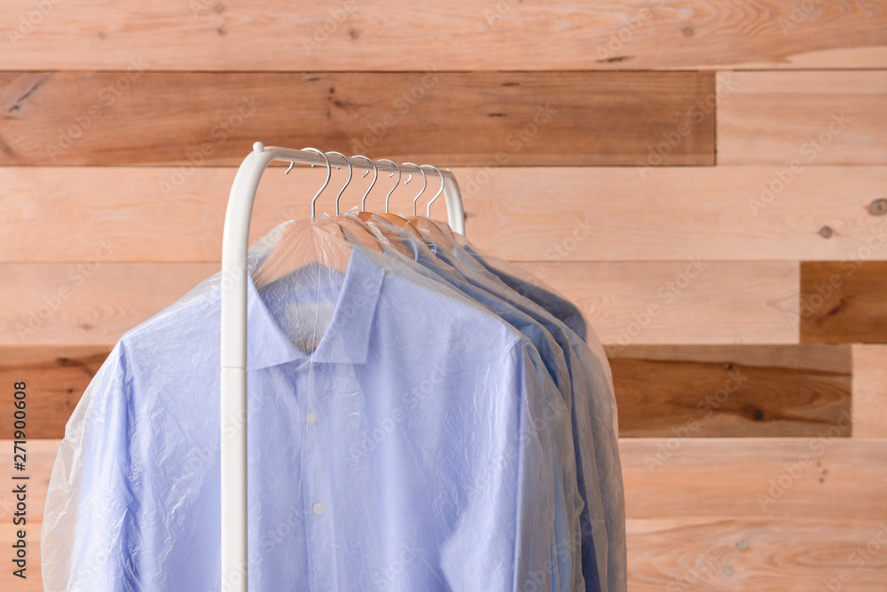 Rack with clothes after dry-cleaning on wooden background