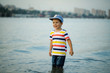 Three year old toddler boy on beach at sunset. Summer family vacation .the child is standing in the water knee-deep in a cap and t-shirt