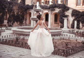 Beautiful bride in pink wedding dress. Outdoor romantic portrait of attractive brunette woman with hairstyle in prom dress with tulle skirt posing by fountain at park.