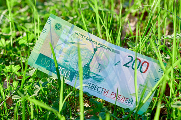 New Russian banknote Two hundred rubles in green grass in clear weather. Cash paper Russian green money.