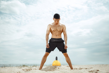 Young healthy man athlete doing exercise with the weight at the beach. Signle male model shirtless training at the river side in sunny day. Concept of healthy lifestyle, sport, fitness, bodybuilding.