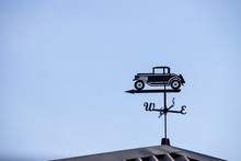 A Device For Displaying The Wind Direction With A Figure In The Form Of An Old Retro Car Is Installed On The Roof Against The Background Of A Clear Blue Sky. Designation North, South, West And East.