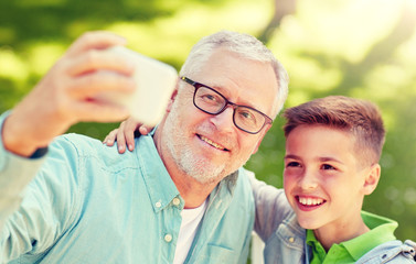 Poster - family, generation, technology and people concept - happy grandfather and grandson with smartphone taking selfie at summer park