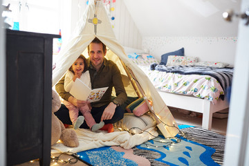 Wall Mural - Portrait Of Single Father Reading With Daughter In Den In Bedroom At Home