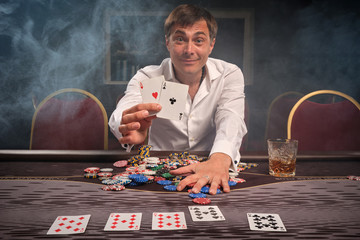 Handsome emotional man is playing poker sitting at the table in casino.