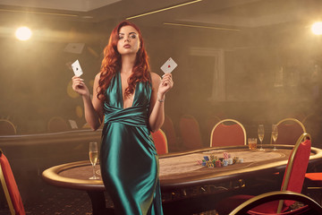 Young beautiful woman is posing against a poker table in luxury casino.