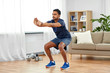 © Syda Productions - sport and healthy lifestyle concept - indian man with fitness tracker exercising and doing squats at home