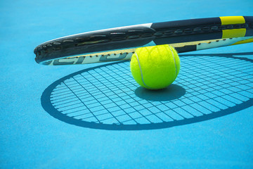 Wall Mural - Summer sport concept with tennis ball and racket on blue hard tennis court. Top view, copy space. Blue and yellow.