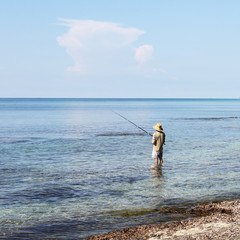 Fisherman with wide oriental style hat and fishing rod. seen from behind.