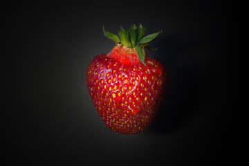 Fresh strawberries in a bowl on wooden table with low key scene.