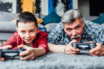 Smiling boy and his grandfather playing video games together at home.