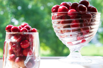 Wall Mural - red sweet cherry in a transparent bowl for ice cream and in a cup on the background of nature 