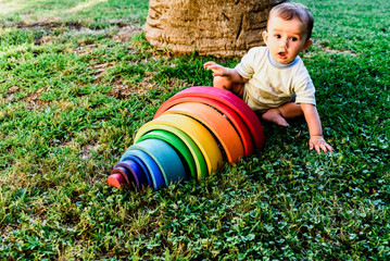 Wall Mural - Baby girl playing with a waldorf material, a rainbow of wood montessori, in nature.