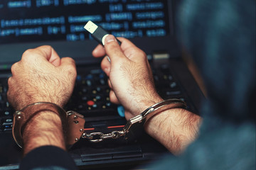 Arrested hacker man handcuffed hands. Prisoner or arrested terrorist, close-up of hands in handcuffs, selective focus. Rear view. Toning