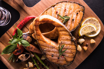 Wall Mural - Grilled salmon fish with seasoning and various vegetables on cutting board on black stone background