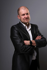 Wall Mural - Serious bald thinking business man with folded arms in suit on grey background. Closeup