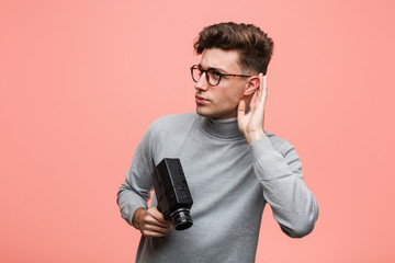 Wall Mural - Young intellectual man holding a film camera trying to listening a gossip.