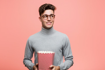 Wall Mural - Young intellectual man holding a popcorn bucket biting fingernails, nervous and very anxious.