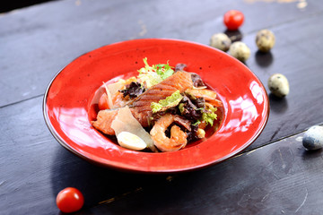 Wall Mural - salad with salmon, shrimps, quail eggs and parmesan on a red plate