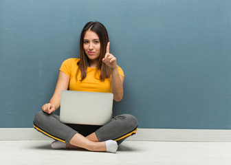 Wall Mural - Young woman sitting on the floor with a laptop showing number one