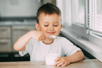 Wall Mural - Adorable little boy eating yogurt in the kitchen in the afternoon