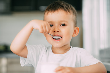 Wall Mural - Adorable little boy eating yogurt in the kitchen in the afternoon