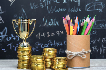 Management of Achievement champion with awards investment in financial concept: Golden trophy on top rows of gold coins, pencils box, blur formula equation blackboard background.Congratulation success