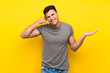 © luismolinero - Handsome man over isolated yellow wall making phone gesture and doubting