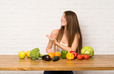 Wall Mural - Young woman with many vegetables extending hands to the side for inviting to come