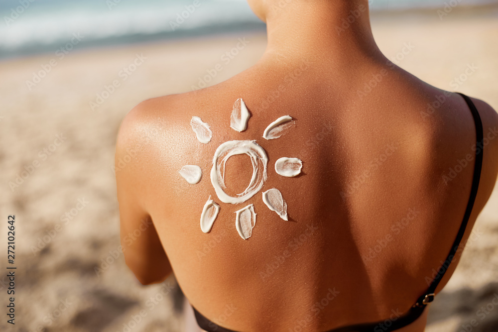 Woman Applying Sun Cream on Tanned  Shoulder In Form Of The Sun. Sun Protection.Sun Cream. Skin and Body Care. Girl Using Sunscreen to Skin. Female Holding Suntan Lotion and Moisturizing Sunblock. - obrazy, fototapety, plakaty 