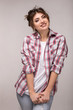 © Victor Studio - Portrait of a young smiling woman in plaid shirt and white t-shirt, standing over gray wall.