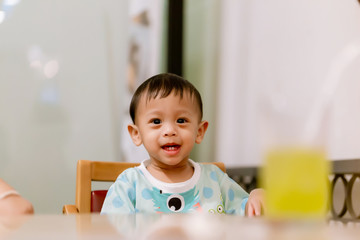 Portrait Of Happy Young Baby Boy In High Chair. Child sitting at empty table.Baby nutrition concept.Food advertisement design. smiling baby sitting on baby Chair.