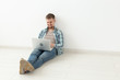 © satura_ - Positive young man in casual clothes surfing the Internet in search of new housing sitting on the floor in an empty room with copy space