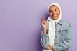 © wayhome.studio  - Carefree optimistic female with toothy smile, being in high spirit, wrapped in white scarf, wears fashionable denim jacket, looks away, poses over purple background, blank space area for information