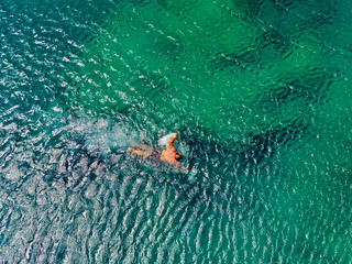 Man swims in crystal clear turquise sea water, sunlight reflects on water surface, view from above.