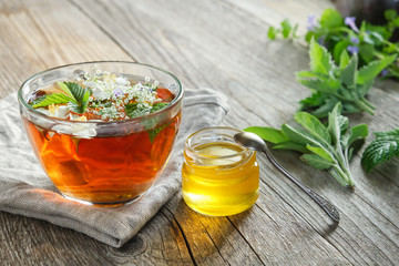 Healthy herbal tea cup, honey jar and medicinal herbs on old wooden table.