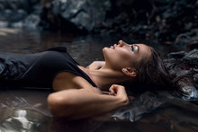 Close Up Photo Of An Attractive Woman With Ideal Beautiful Face Enjoying Nature Lying On Her Back In Darkness Lost In Thought Thinking Deeply Amongst Dark Forest And Black Stones