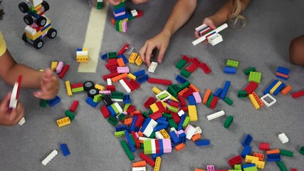 Wall Mural - Hand of kids playing toy constructor on the floor. Multicolored block toys in classroom, top view. Developing game for preschool kids.